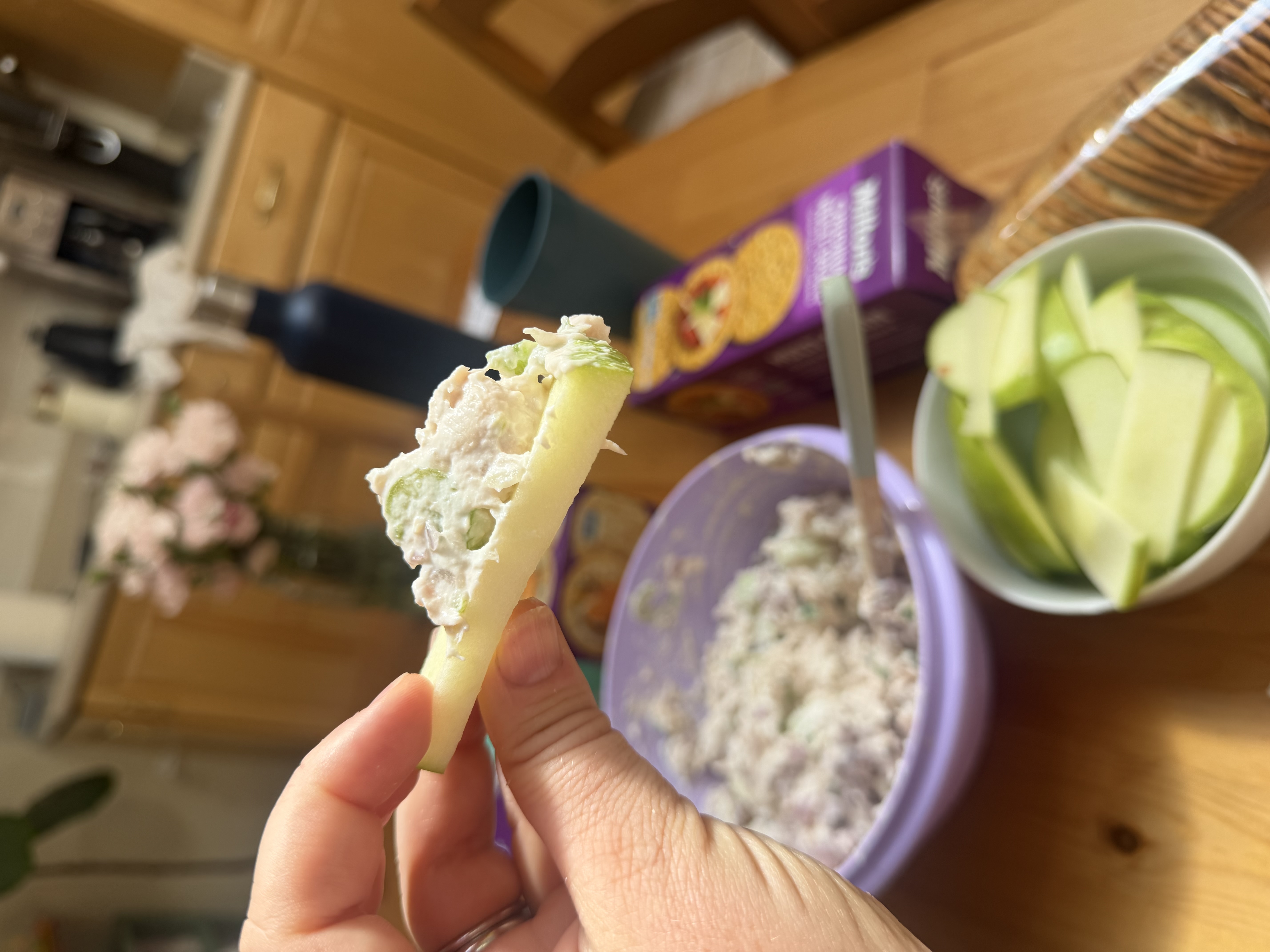 A hand holding a green-apple slice topped with chicken salad