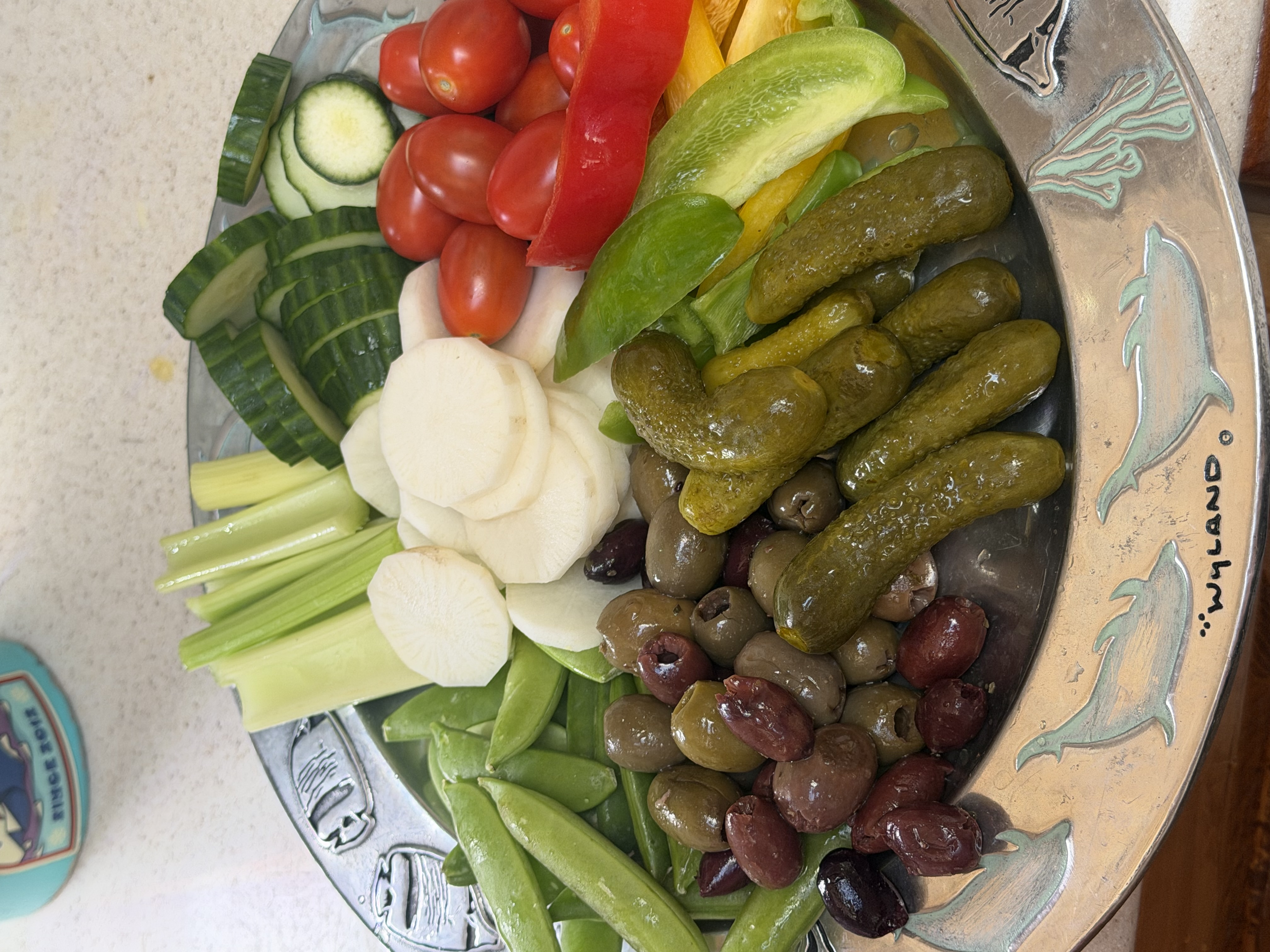 A large silver dolphin platter piled with crunchy cold vegetables, olives, and pickles